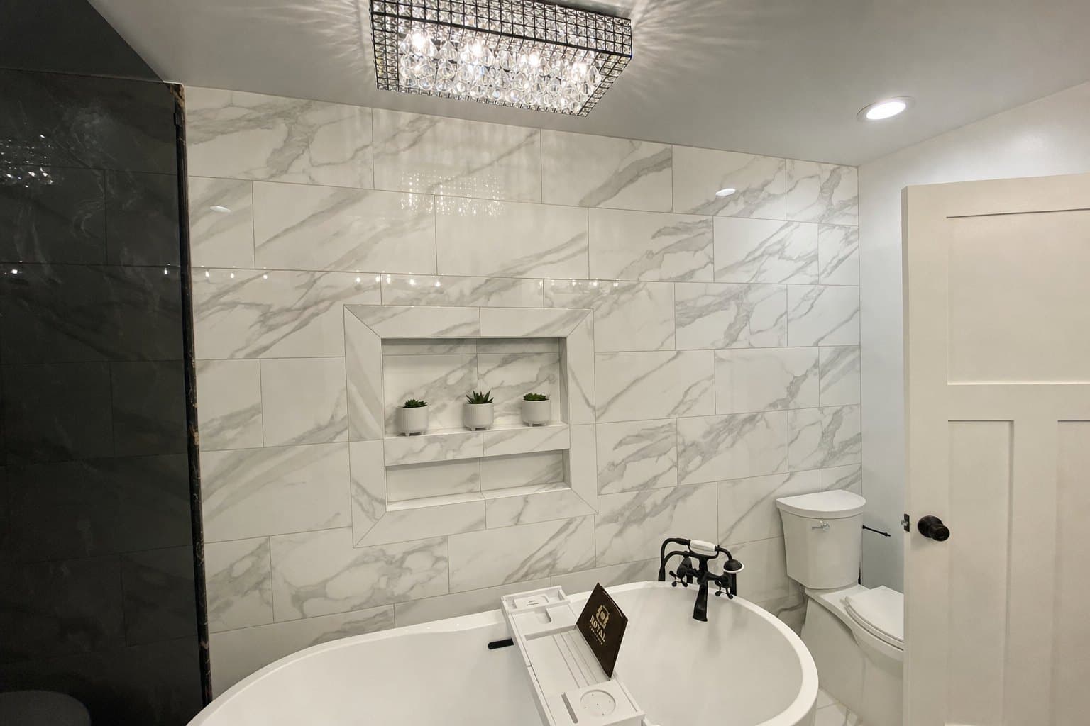 Custom marble bathroom with freestanding tub, crystal chandelier, and recessed niche shelving
