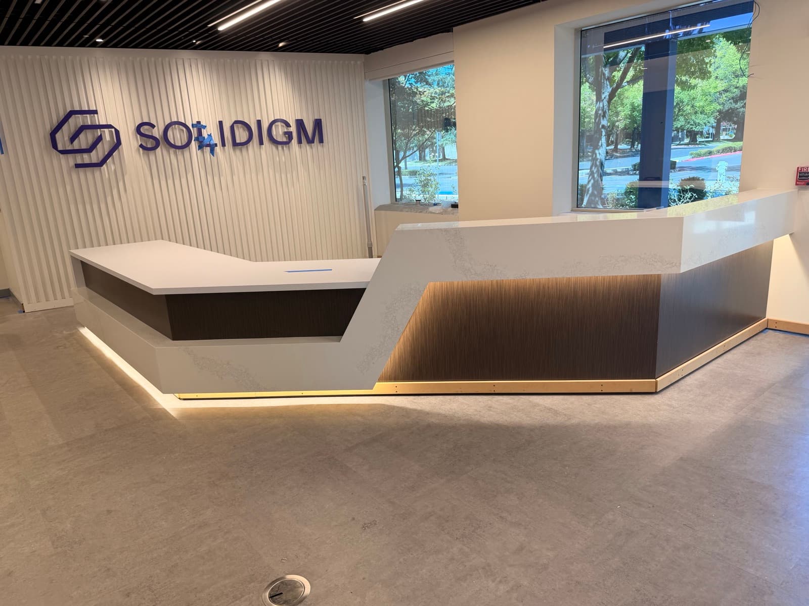 Commercial office reception desk with angular quartz countertop, waterfall transaction ledge, and LED-lit toe kick