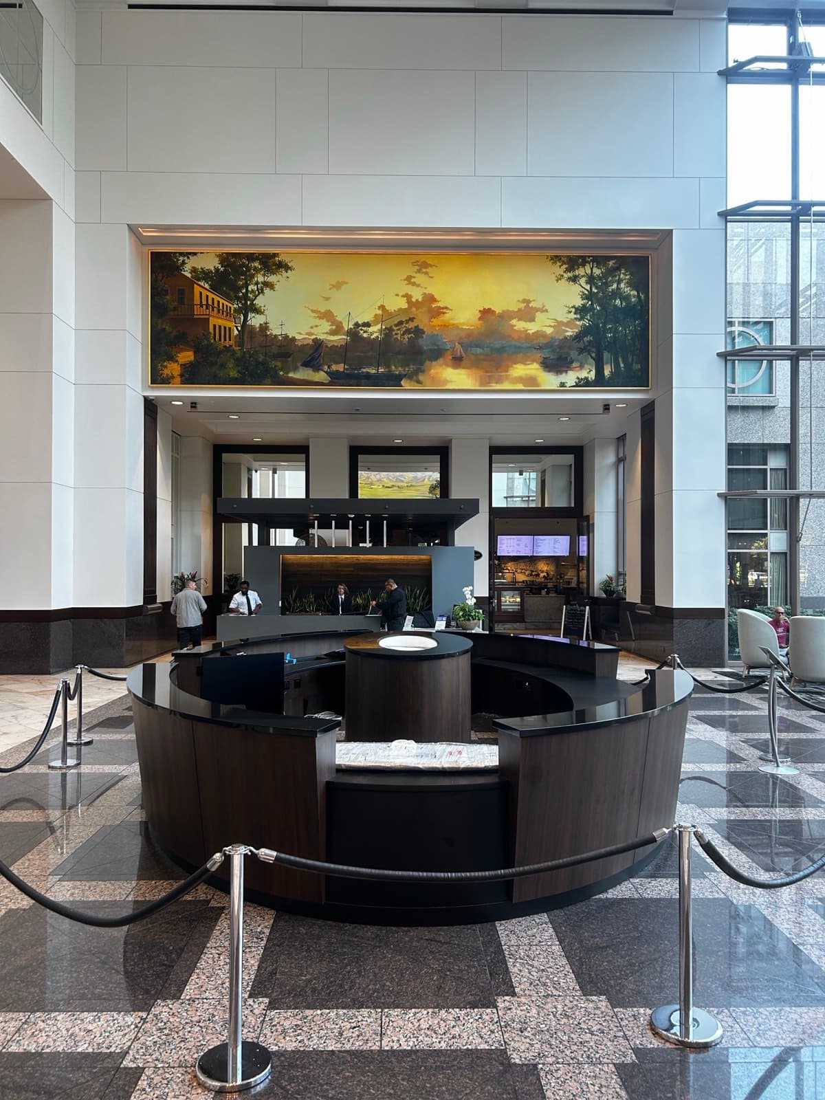 Curved walnut-panel lobby desk with black stone countertops and a central stone-topped pedestal